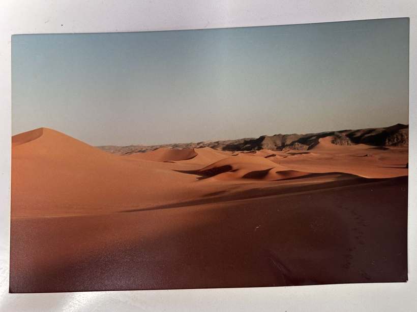 Une grande dune au soleil couchant, des rochers noirs au pied.