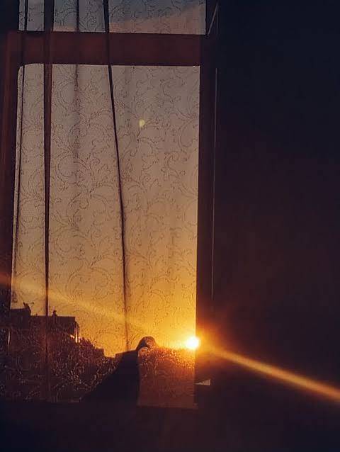 Un rideau devant une fenêtre, le soleil couchant derrière.