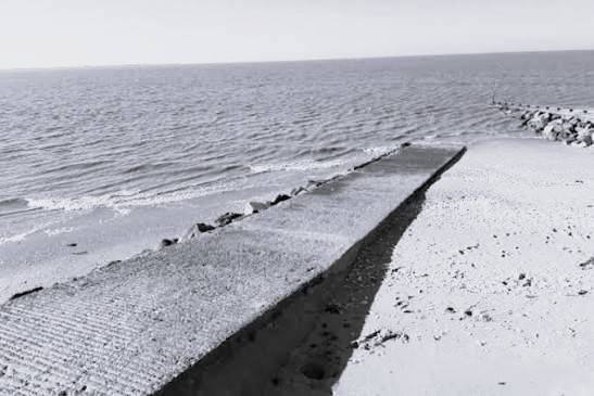 Noir et blanc : une cale qui descend vers la mer, sur le sable.