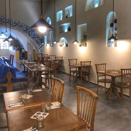Une salle de restaurant voûtée, tables en bois et lampes suspendues.