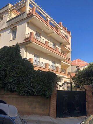 Un immeuble derrière un haut mur et un portail en fer.